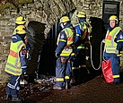 Menschen in Einsatzkleidung stehen am Eingang zu einem Stollen. Es ist dunkel.