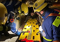 Mehrere Einsatzkräfte knien neben einem gelben Kunststoffbrett, einem Spine-Board, mit dem Verletzte transportiert werden können.