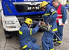 Drei Menschen stehen vor einem Lastwagen. Zwei bringen einen Greifzug am Fahrzeug an.