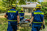 Vier Menschen in Einsatzkleidung des Technischen Hilfswerks tragen einen Schleifkorb auf ein Gebäude zu.