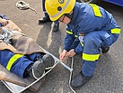 Ein Mensch in Einsatzkleidung hockt neben einer Krankentrage und befestigt ein Seil daran. 