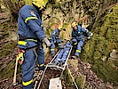 Einsatzkräfte stehen am Ausgang einer Höhle. Zwischen ihnen steht ein Metall-Schleifkorb zum Transport Verletzter.