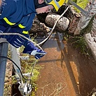 Ein Mensch in Einsatzkleidung lässt eine Tauchpumpe an einem Seil in ein Behältnis mit Wasser herab.