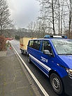 Ein blauer Transporter steht auf einer Straße. Hinter sich hat er einen hellen Anhänger. 