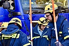 Menschen in Einsatzkleidung halten orange-weiße Stäbe in den Händen. Im Hintergrund steht ein blaues Fahrzeug.