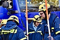 Menschen in Einsatzkleidung halten orange-weiße Stäbe in den Händen. Im Hintergrund steht ein blaues Fahrzeug.