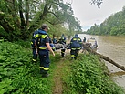 Einsatzkräfte des Technischen Hilfswerks tragen eine Krankentrage am Flussufer entlang in Richtung eines Boots, das auf dem Wasser liegt.