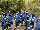 Eine Gruppe von Menschen in Einsatzkleidung steht vor Bäumen. 