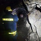 Ein Mensch in Einsatzkleidung steht in einer Höhle. Es ist dunkel, nur eine Taschenlampe sorgt für etwas Beleuchtung.