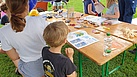 Kinder und Eltern sitzen an einem Tisch, auf dem Malbücher und Stifte liegen.