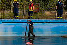 Eine Helferin des Technischen Hilfswerks läuft in Wathose durch ein Schwimmbecken. Am Rand des Beckens stehen weitere Menschen in Einsatzkleidung.