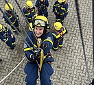 Eine Frau in Einsatzkleidung hängt mit einem Sicherungsgurt an einem Seil. Weiter unterhalb von ihr stehen andere Menschen in Einsatzkleidung.